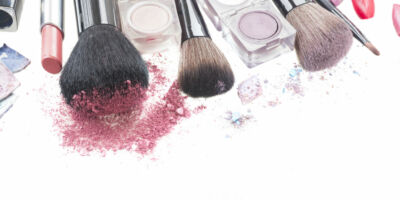 border of  make up brushes, lipsticks and  eye  shadows with crumbles close up  isolated on white background