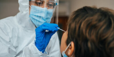 Close up of female health Professional in PPE introducing a nasal swab to a senior female patient at her house. Rapid Antigen Test kit to analyze nasal culture sampling while coronavirus Pandemic.